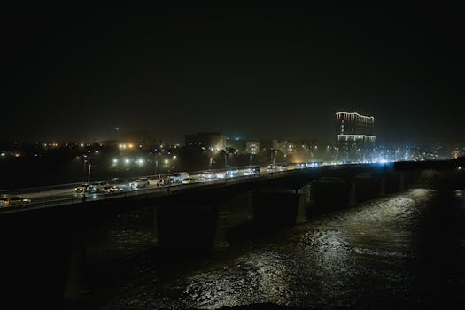 A night scene featuring a bridge with bustling traffic and illuminated cityscape in the background.