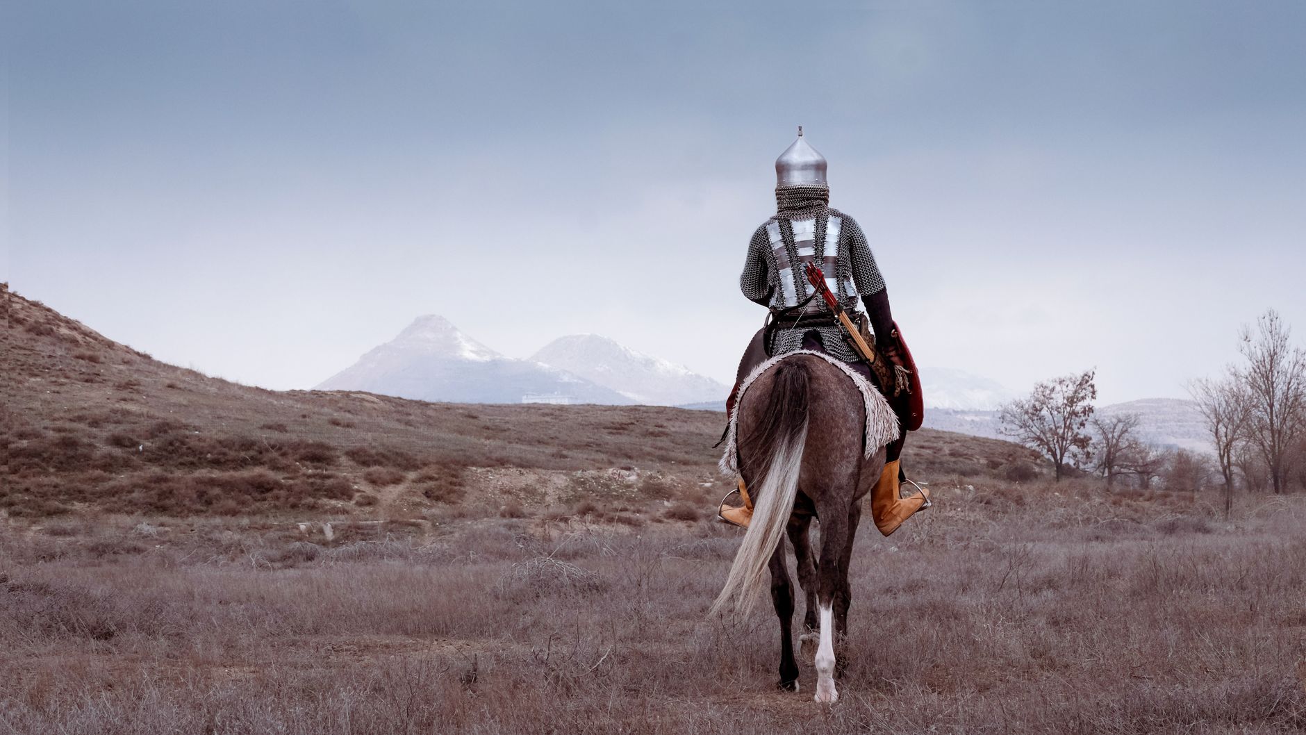 A Turkish warrior in historical armor on horseback faces a vast landscape in Konya, Türkiye.