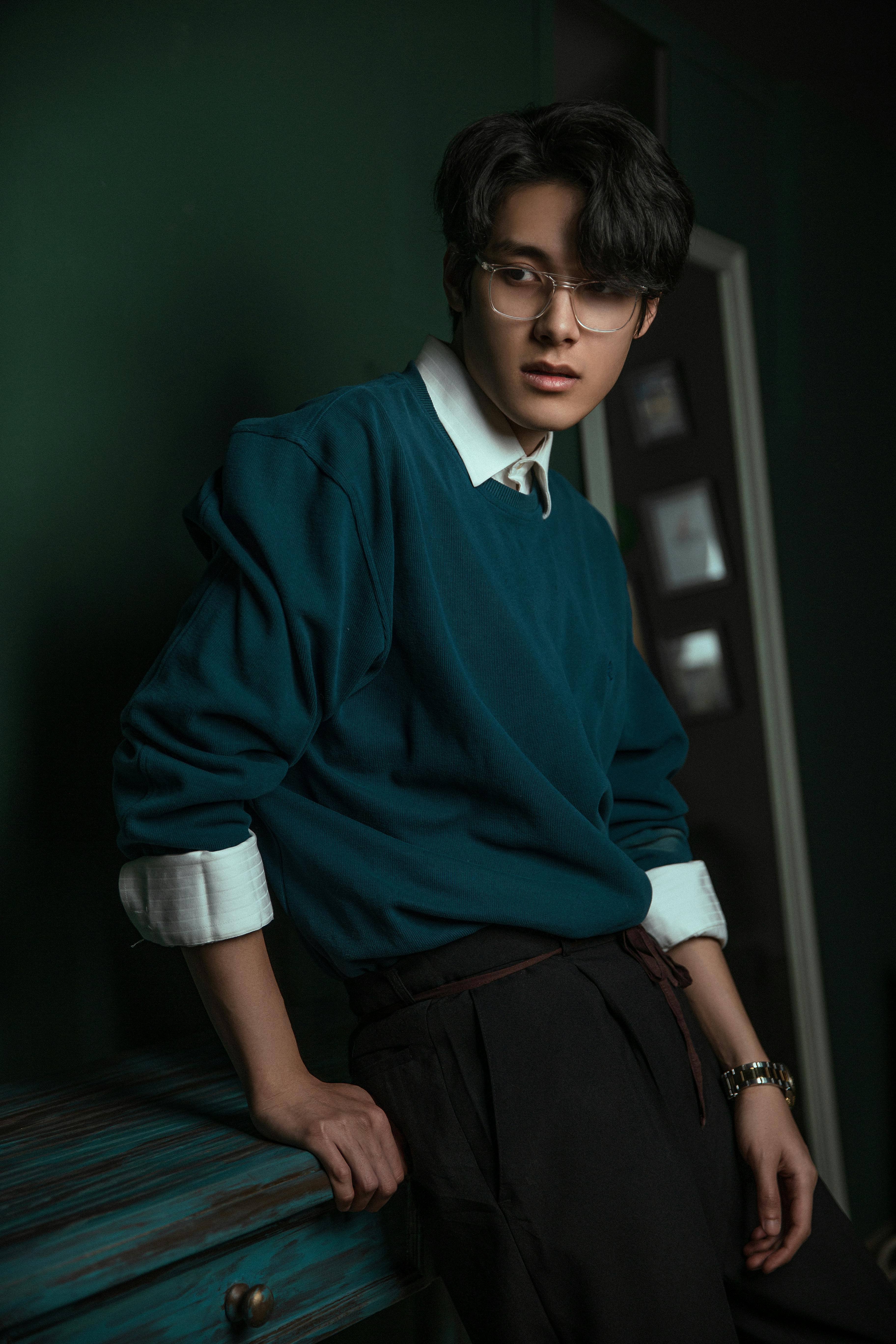 Gratis Un giovane adulto con gli occhiali e un abbigliamento comodo posa in un ambiente interno, creando un'atmosfera calda ed elegante. Foto a disposizione