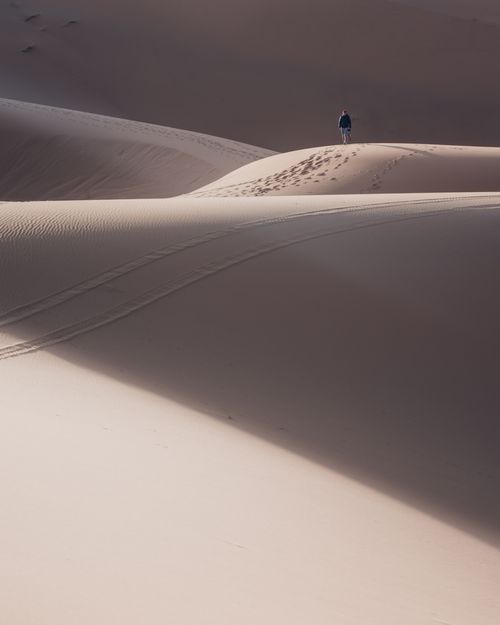 Free A solitary figure walks atop a vast, serene desert sand dune under clear skies. Stock Photo