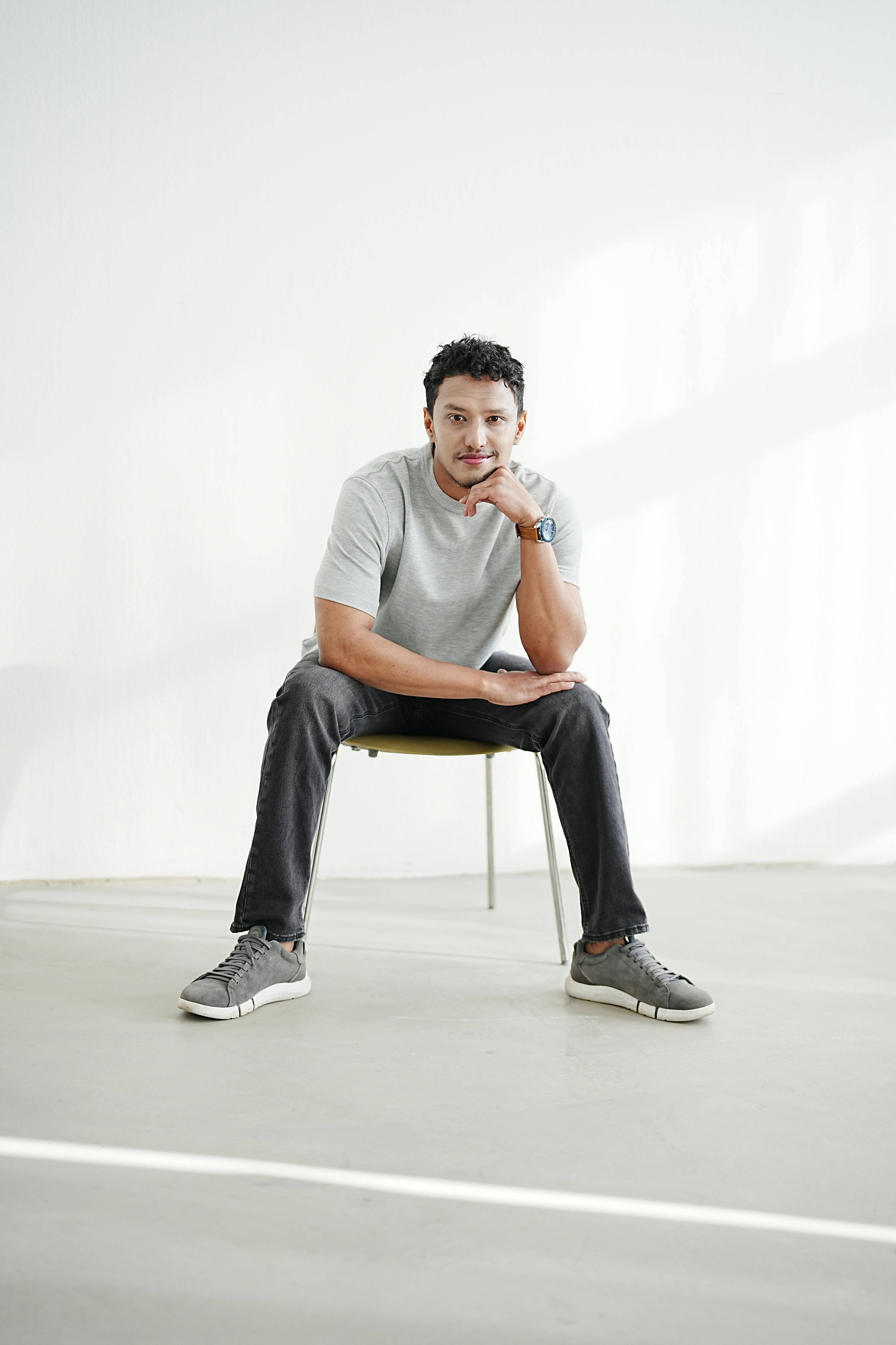 Gratis Un giovane rilassato, seduto con aria disinvolta su una sedia in uno studio ben illuminato. Foto a disposizione