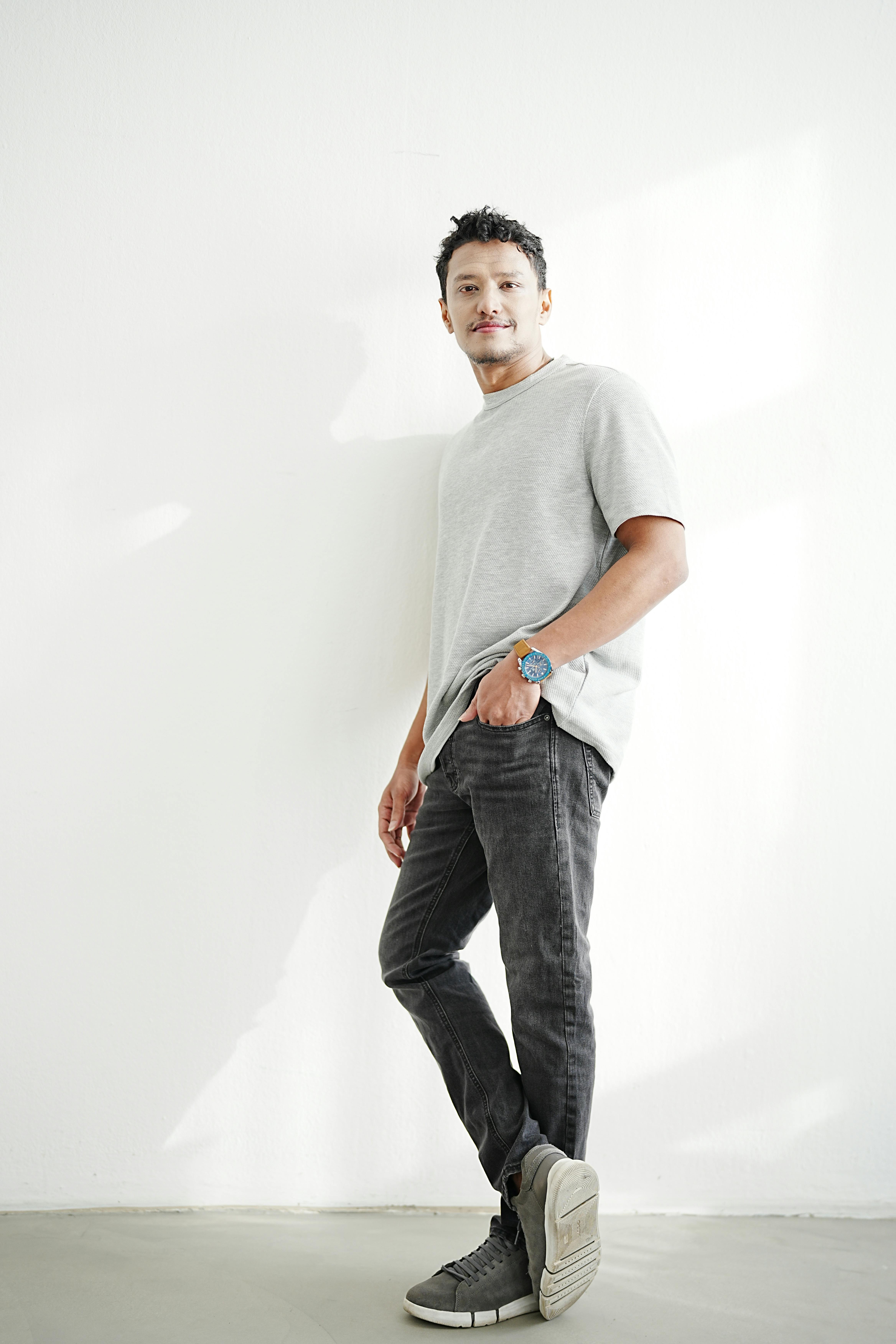 A relaxed pose of an adult man in casual attire inside a bright room.