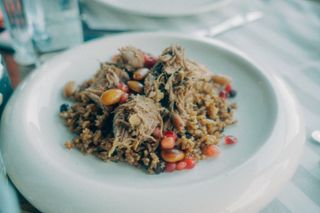 A close-up of a savory meat and rice pilaf garnished with nuts and pomegranate seeds.