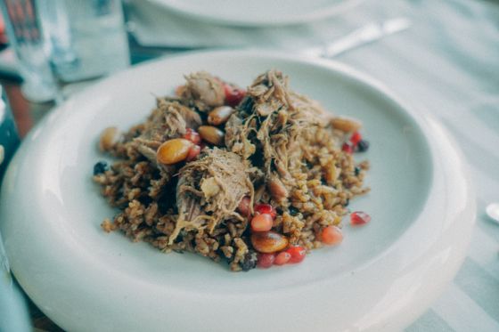 Bulgur pilaf topped with shredded lamb, chickpeas and pomegranate seeds on a white plate
