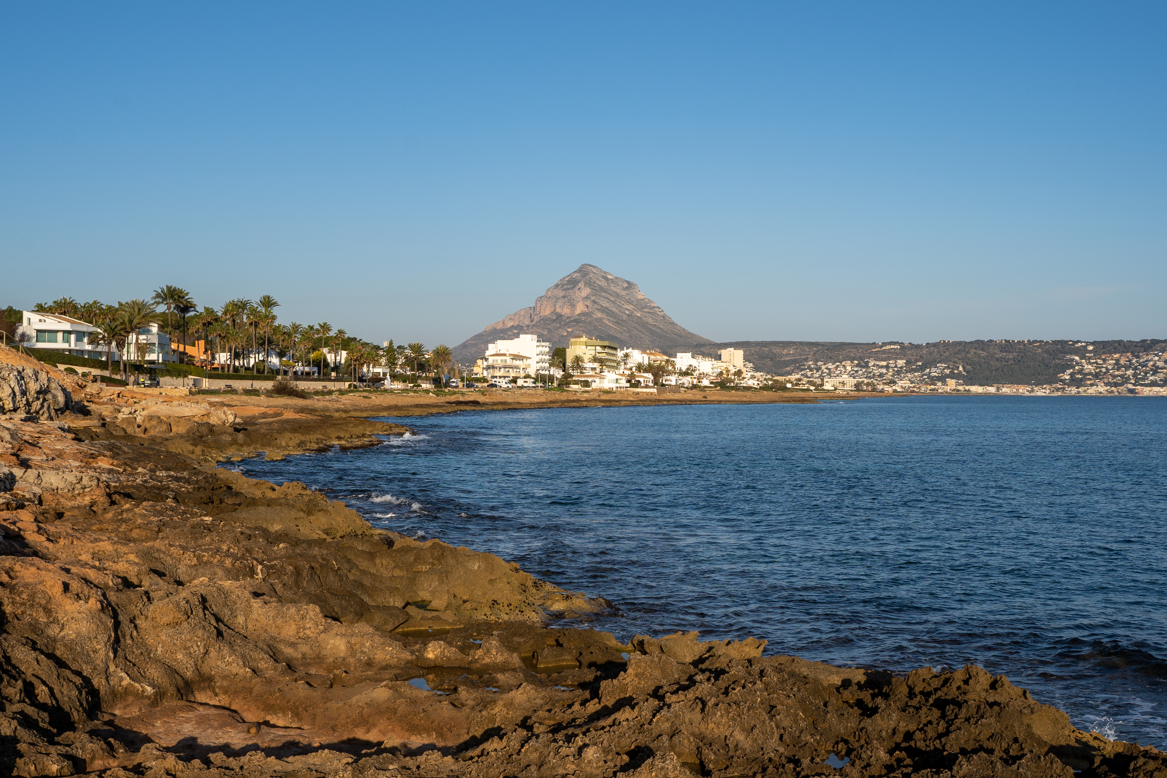 Beautiful coastal landscape of Moraira, Spain with rocky shoreline and distant mountain view.