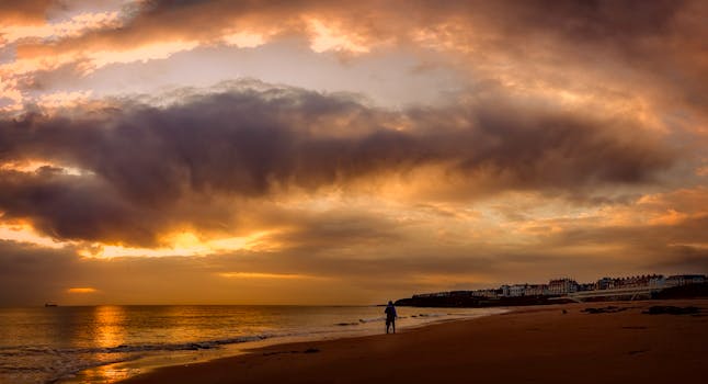 日落为海滩涂上温暖的色调，云层在上方盘旋，海浪轻轻拍打着海岸