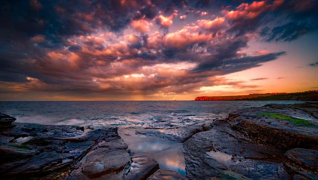 Stunning view of a sunset over the ocean with dramatic clouds and rocky shore.