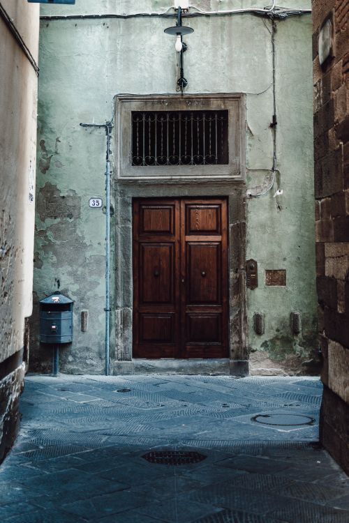 Free A rustic wooden door in an old stone building along a narrow alley, showcasing classic European architecture. Stock Photo