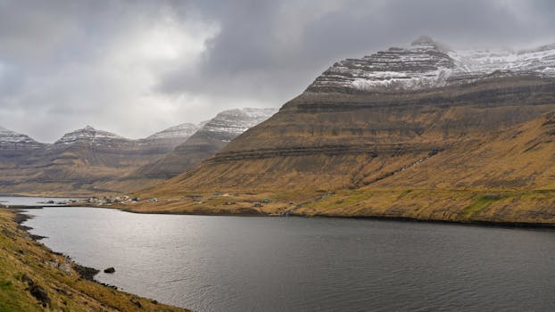 Breathtaking view of snow-capped mountains and fjord in the Faroe Islands under a cloudy sky.