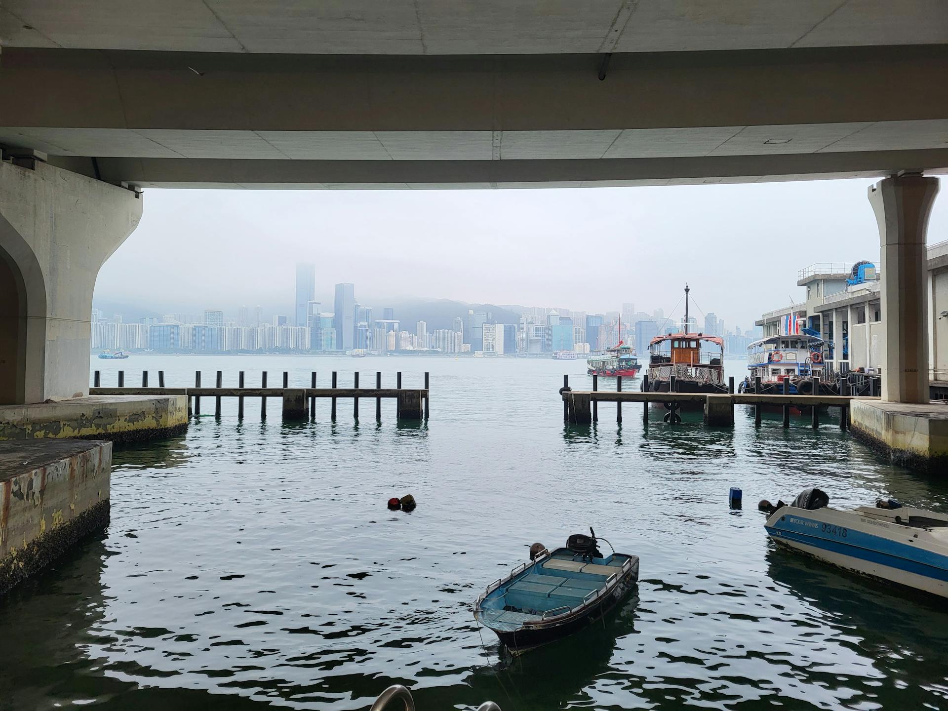 View of Hong Kong skyline framed by a bridge, overlooking boats and harbor.