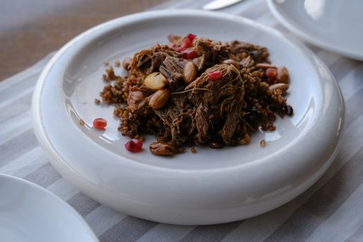 Close-up of a Turkish dish featuring lamb, nuts, and pomegranate seeds on a white plate.