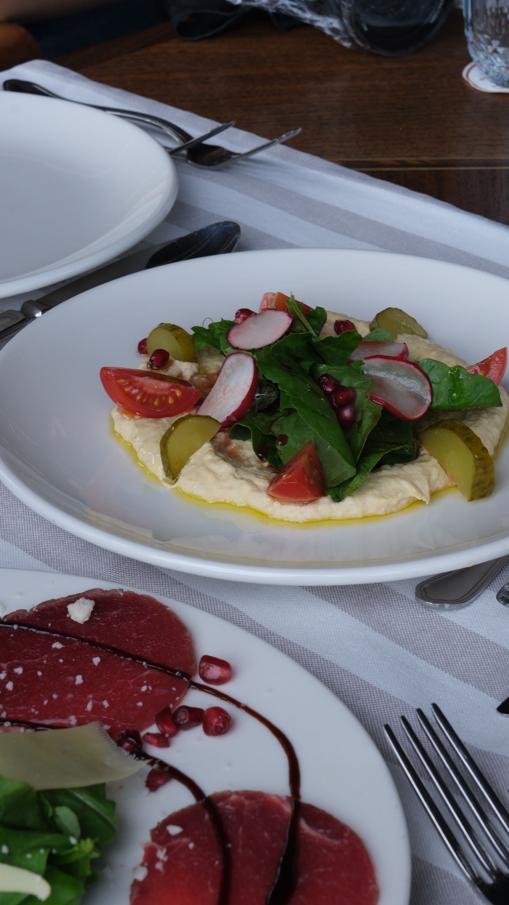 Delicious gourmet salad with radishes and pickles served alongside delicate prosciutto slices on an elegant table setting.