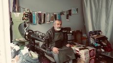 Elderly shoemaker in his workshop, sitting by a sewing machine.