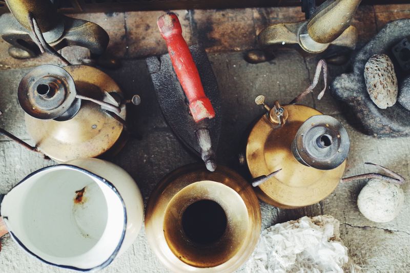 Top view of vintage brass and iron antiques including lamps and an iron on a textured surface.