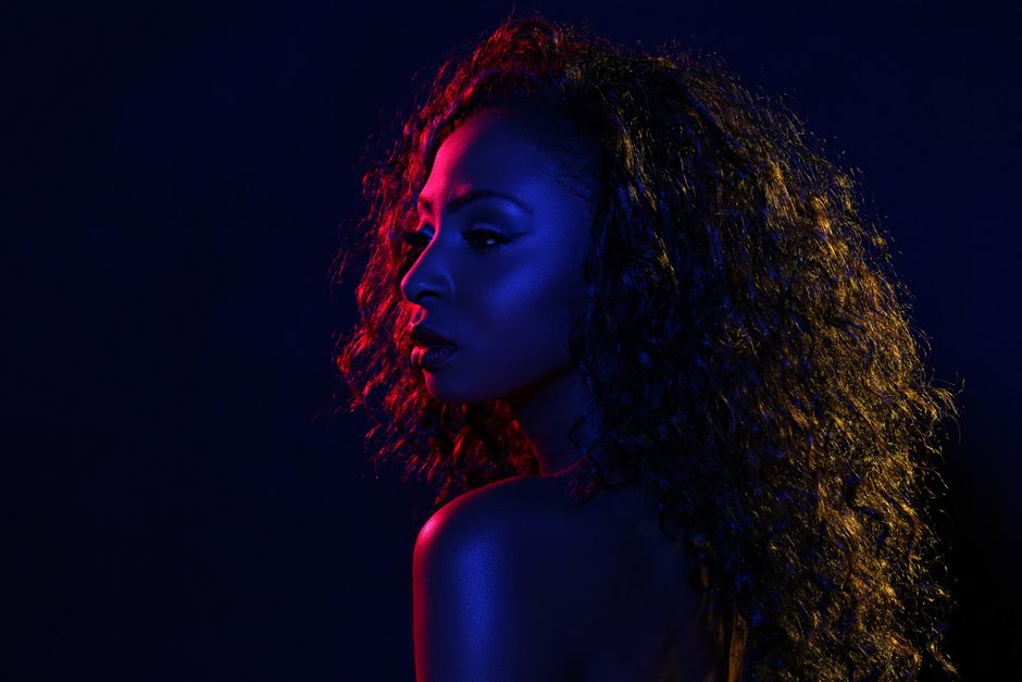 Stylish portrait of a woman with curly hair in colorful dramatic lighting. Perfect for editorial use.