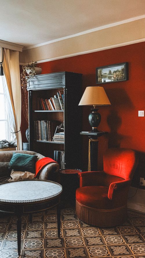 Free Charming vintage reading nook with red accents, bookshelves, and lamp. Stock Photo