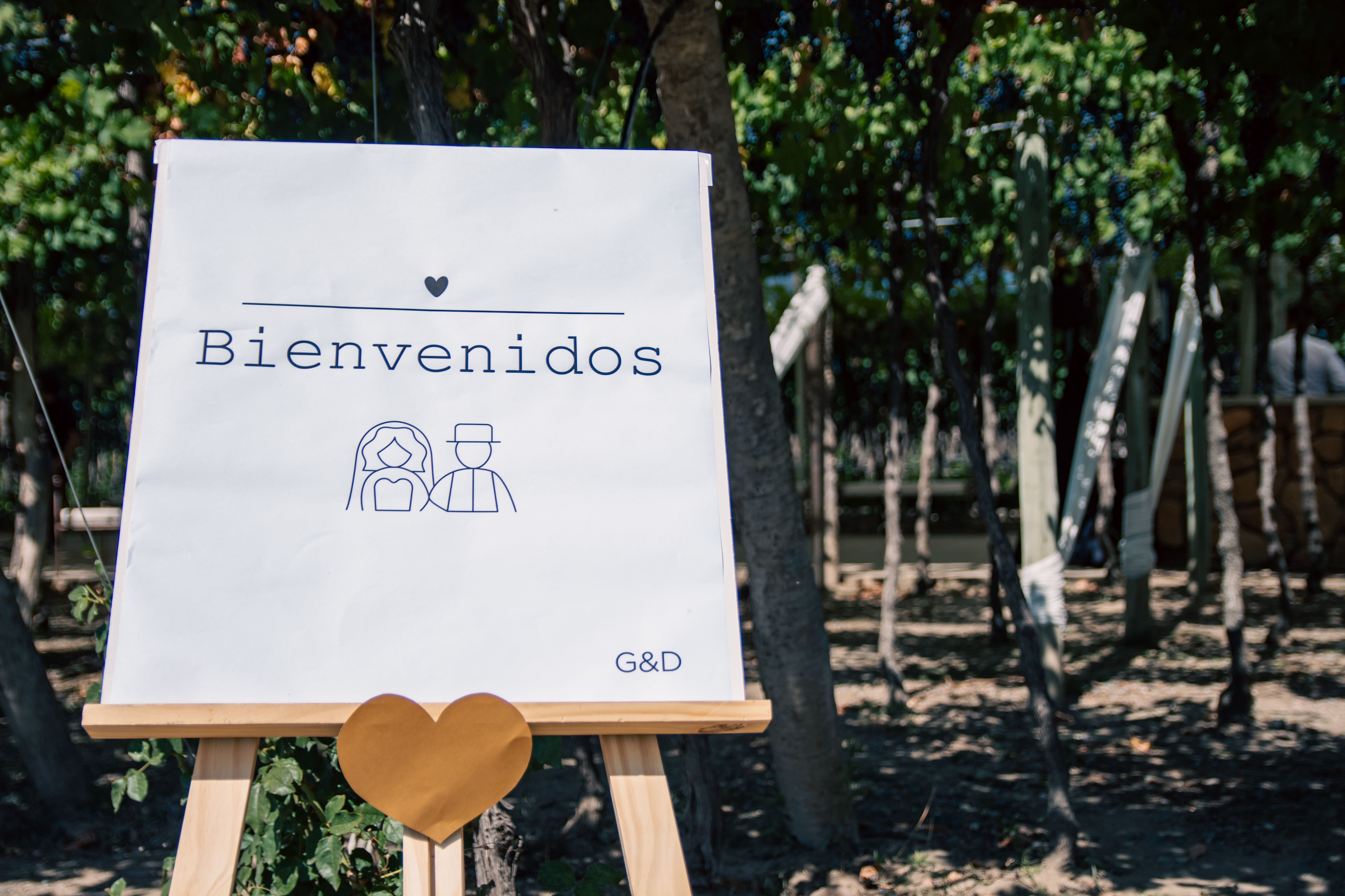 Welcome sign for outdoor wedding with trees and heart decor.