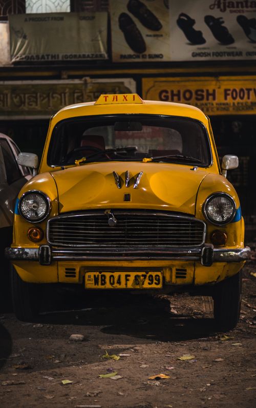 Free A classic yellow Indian taxi parked under neon lights at night in the city. Stock Photo