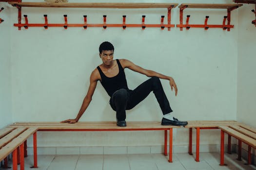 A stylish individual strikes a pose on a bench in a minimalist locker room setting.
