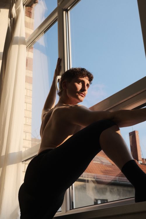 Free Man striking dynamic pose by a sunny window in Berlin, showcasing athleticism. Stock Photo