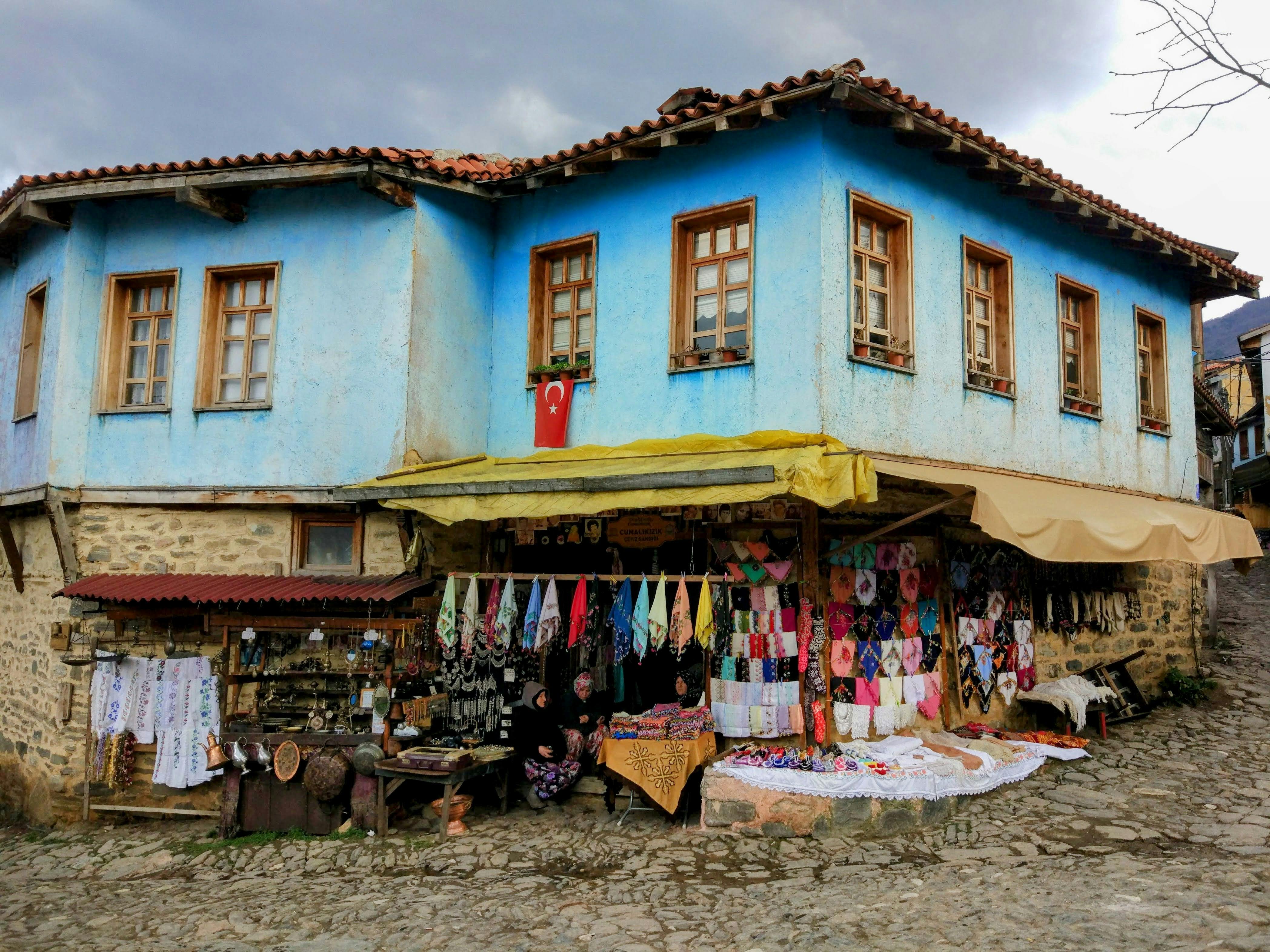 Colorful traditional market in front of a blue Ottoman-style house in Cumalıkızık, Bursa.