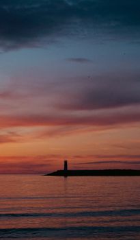 Beautiful silhouette of a lighthouse against a vivid sunset sky over calm sea waters.