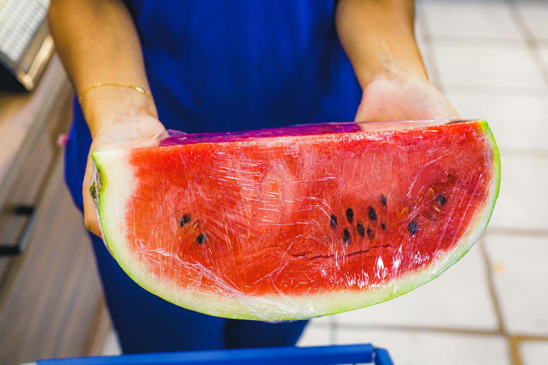 Close-up of a juicy watermelon slice wrapped in plastic held by a person.