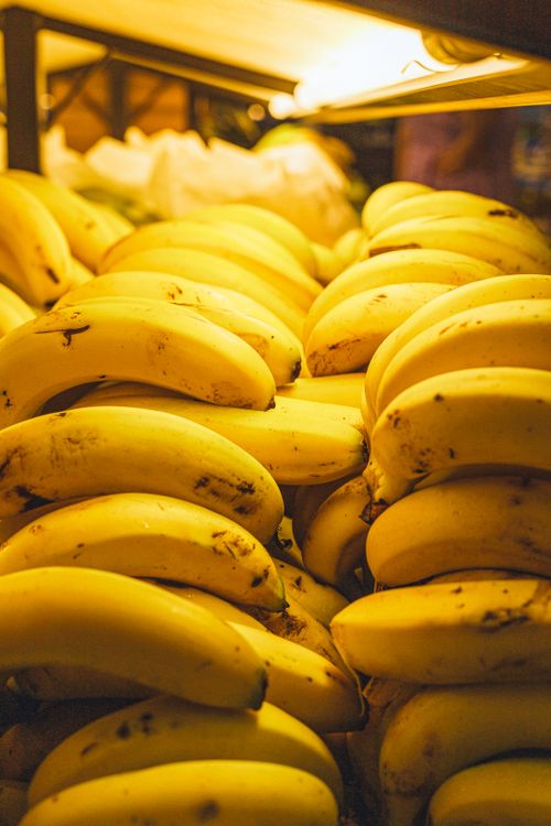 Free Close-up of ripe yellow bananas stacked in a market display under warm lighting. Stock Photo