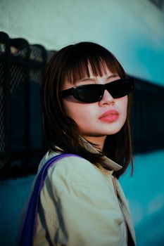 一位年轻女子戴着墨镜，在蓝色背景下自信地摆姿势