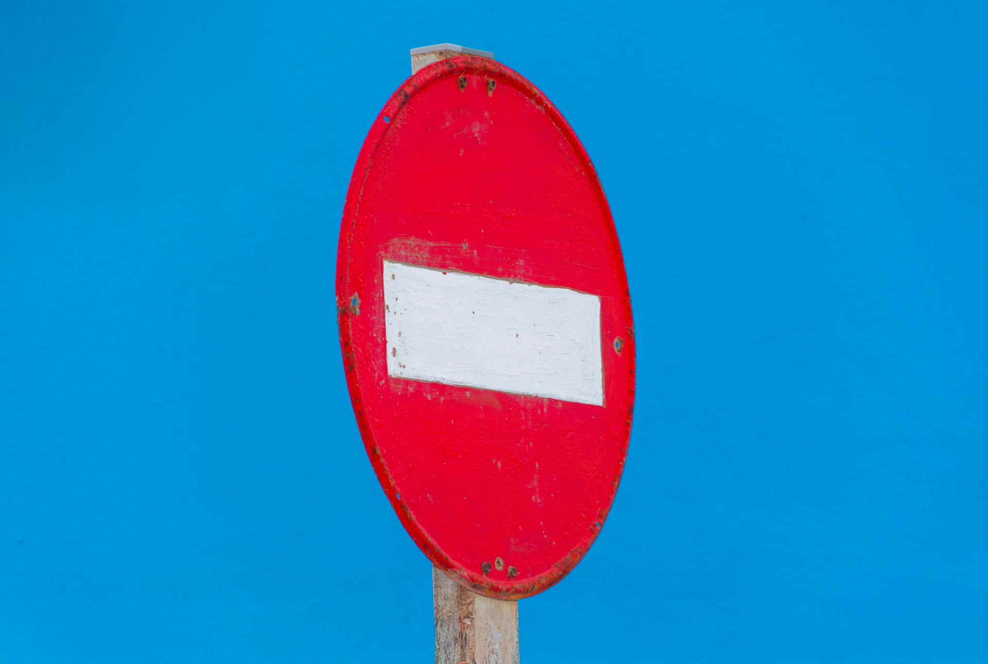 Close-up of a red 'No Entry' sign on a wooden post against a vivid blue background.