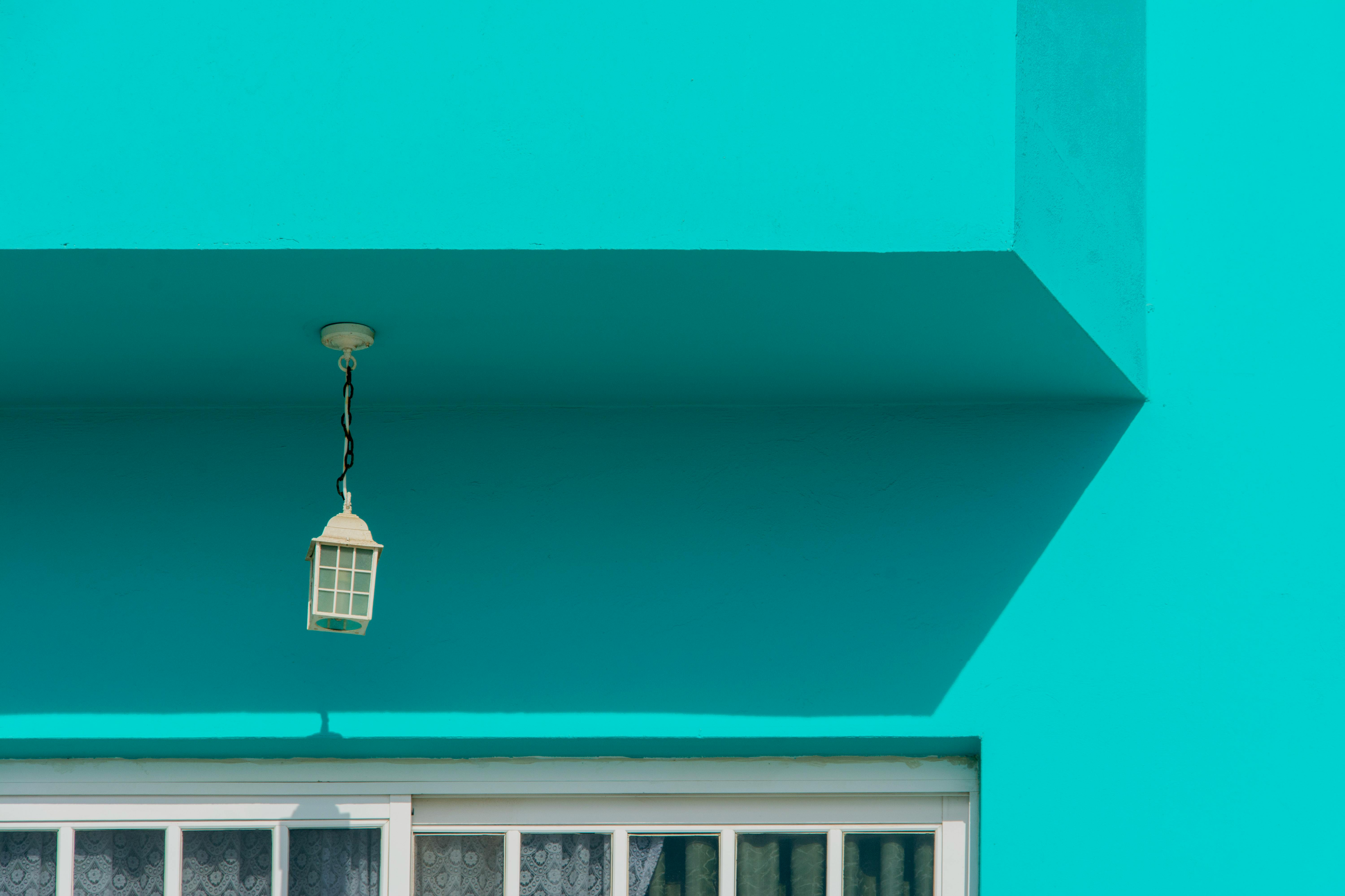 A striking turquoise building facade featuring a hanging lantern and window in Arinaga, Spain.