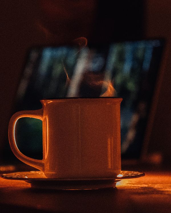 A steaming enamel mug on a saucer, lit warm against the dark