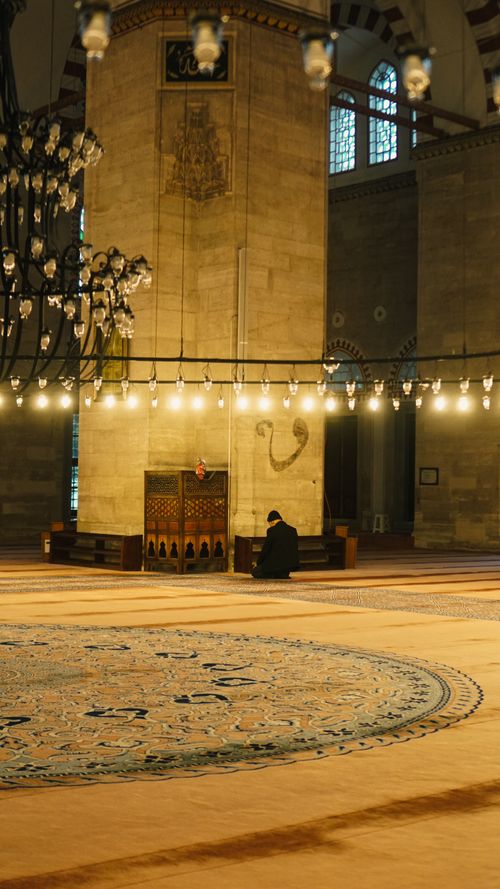 Free A single person in quiet reflection inside a grand mosque with stunning architectural details. Stock Photo