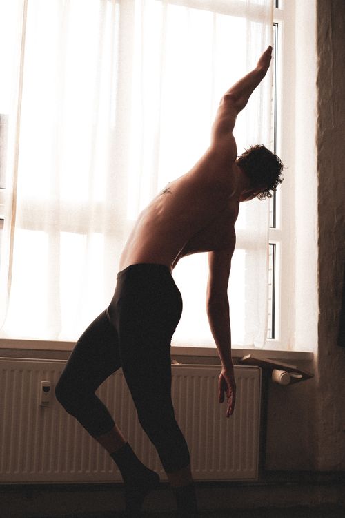 Free A man performs a stretching exercise indoors, silhouetted against a bright window. Stock Photo