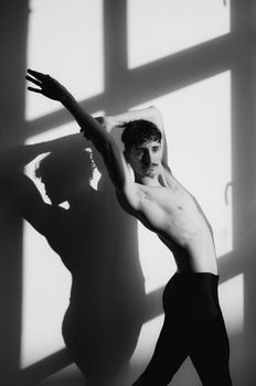 Artistic black and white photo of a male dancer striking a pose against a shadowed wall.