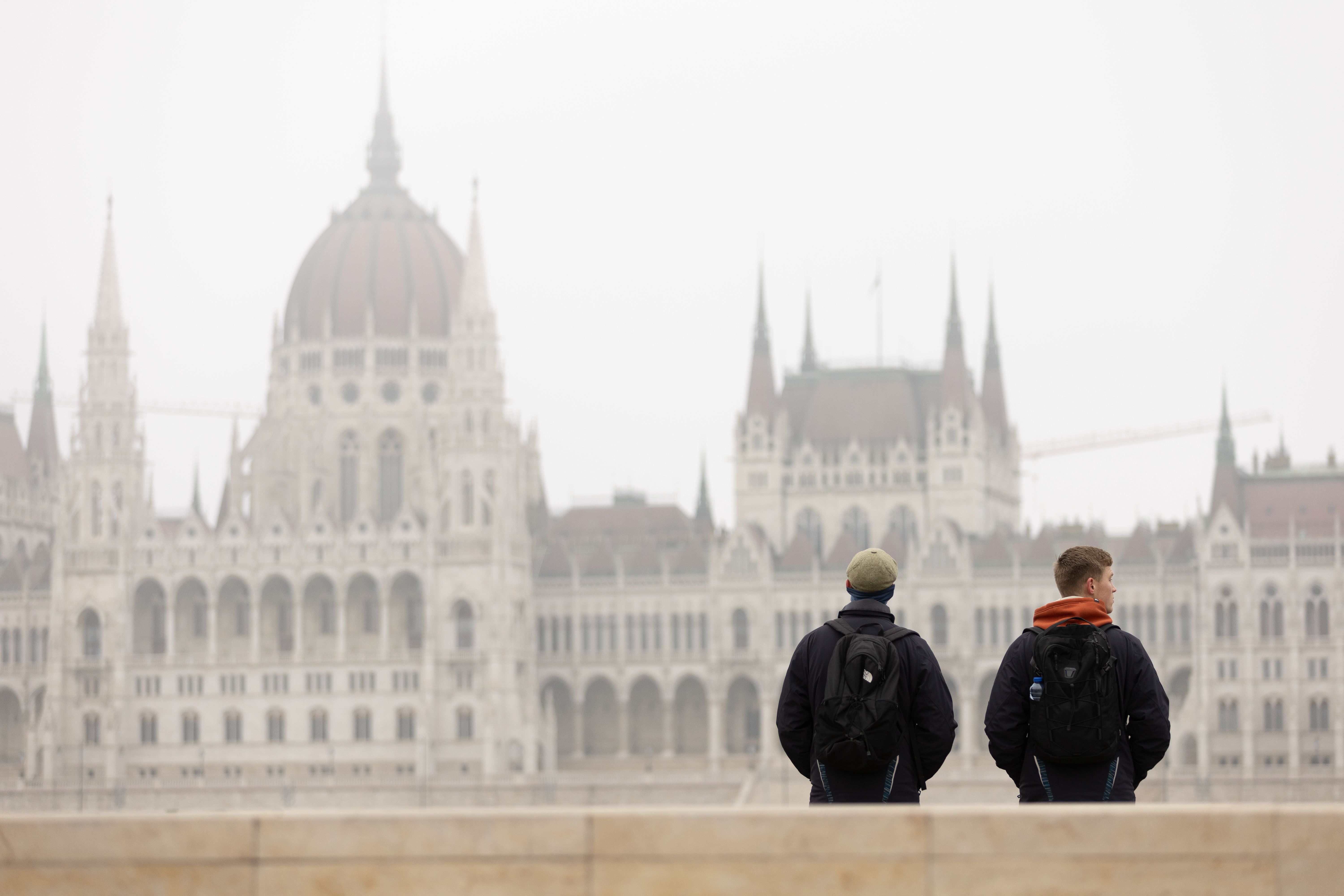 Two tourists with backpacks admire the Hungarian Parliament Building in Budapest on a foggy day.