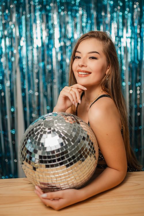 Free Joyful woman holding a disco ball with a sparkling background, capturing festivity and glamour. Stock Photo