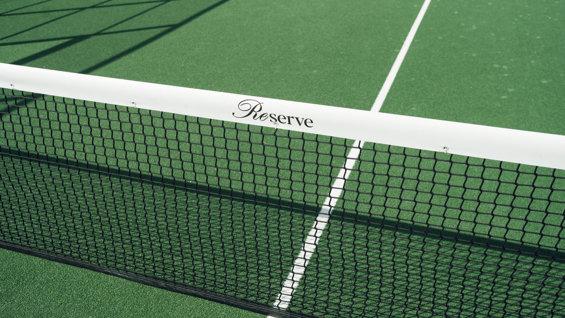 Close-up of a tennis court net displaying 'Reserve' text. Bright green surface.