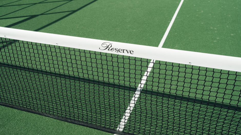 Close-up of a tennis court net displaying 'Reserve' text. Bright green surface.