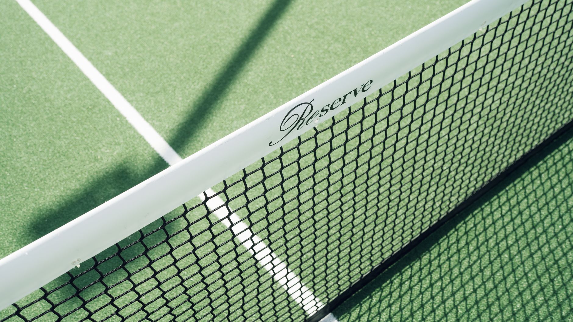 Close-up of a tennis net on a green court with 'Reserve' label casting a shadow.