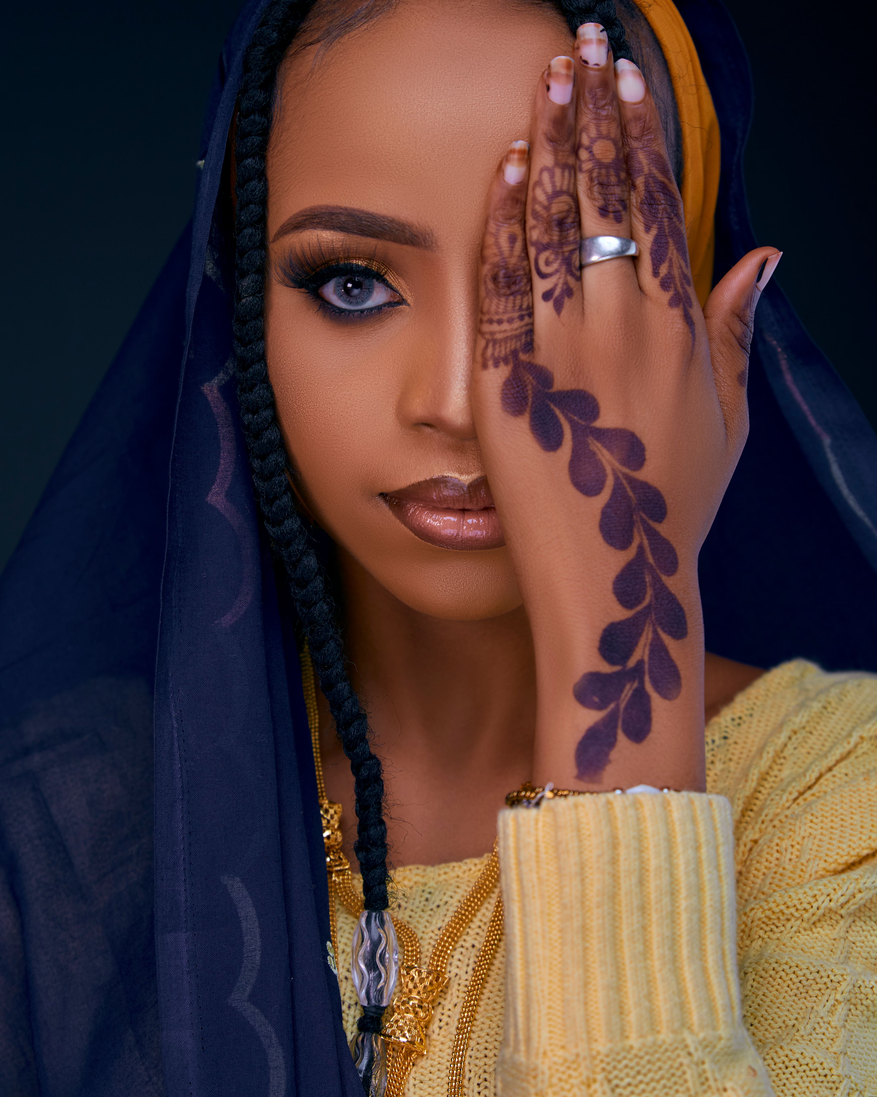 Striking portrait of a woman in traditional attire with elaborate henna design on hand.