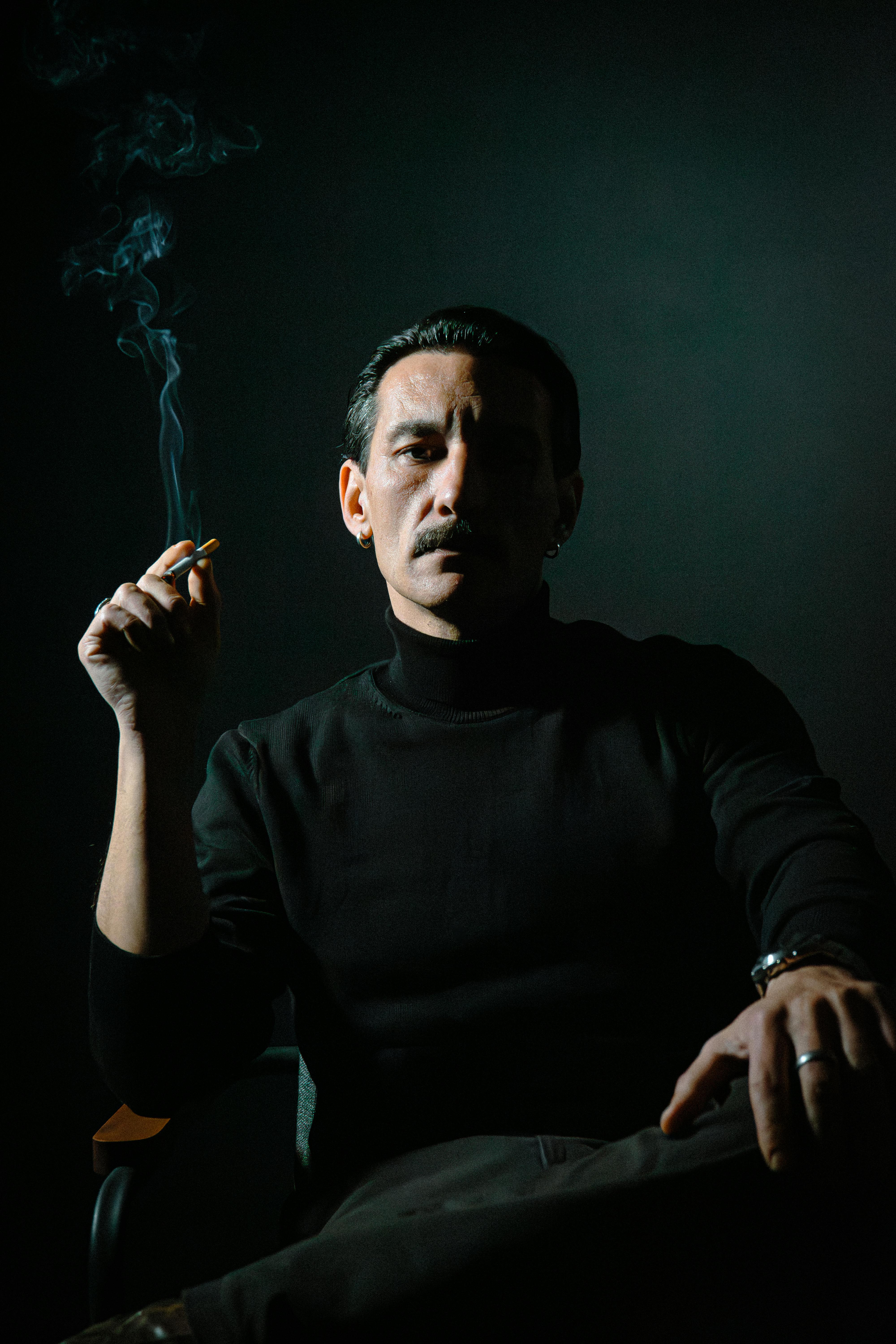 Intense portrait of a man smoking in dramatic low lighting, creating a mysterious atmosphere.