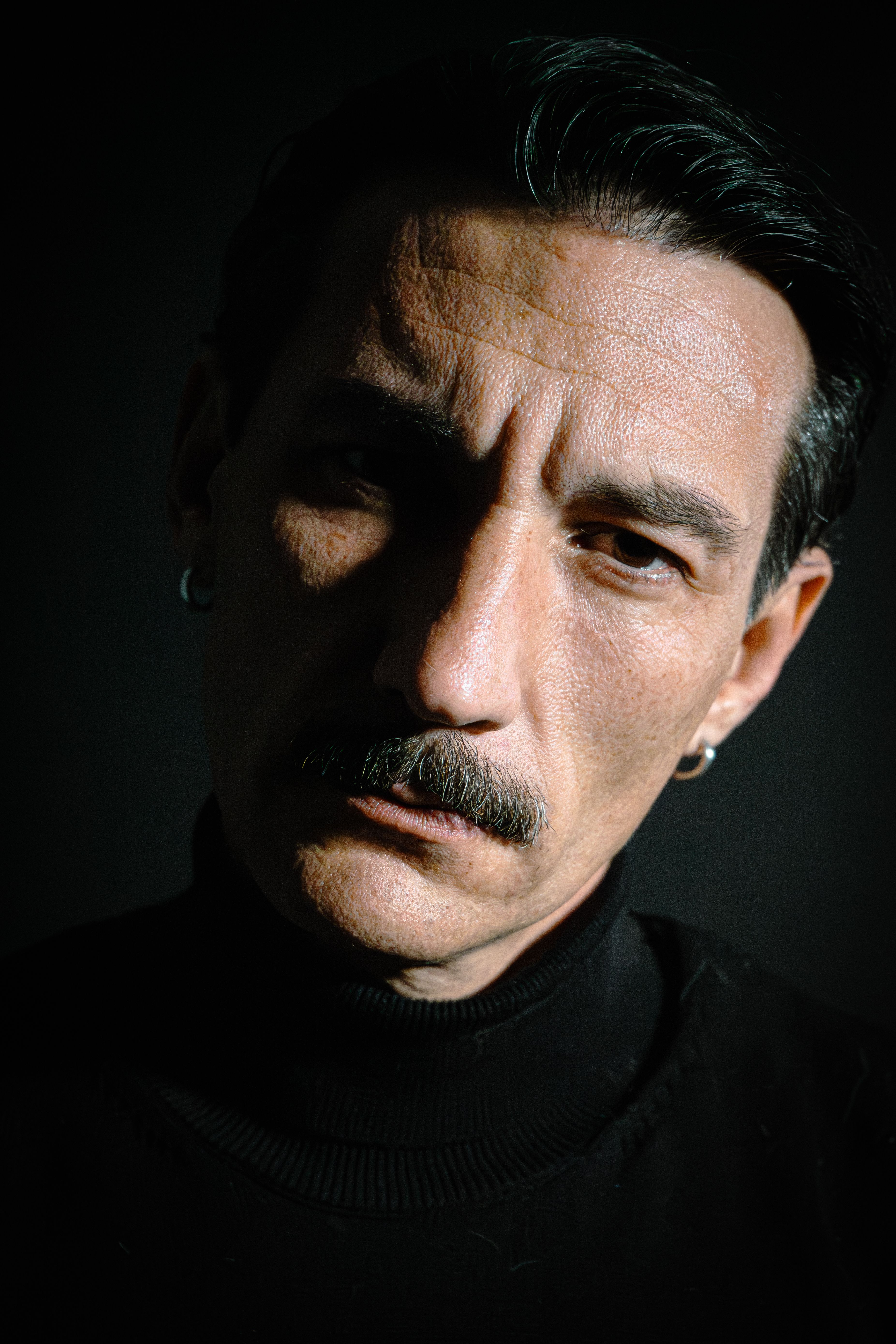 Intense portrait of a man with a mustache against a dark background. Strong lighting.