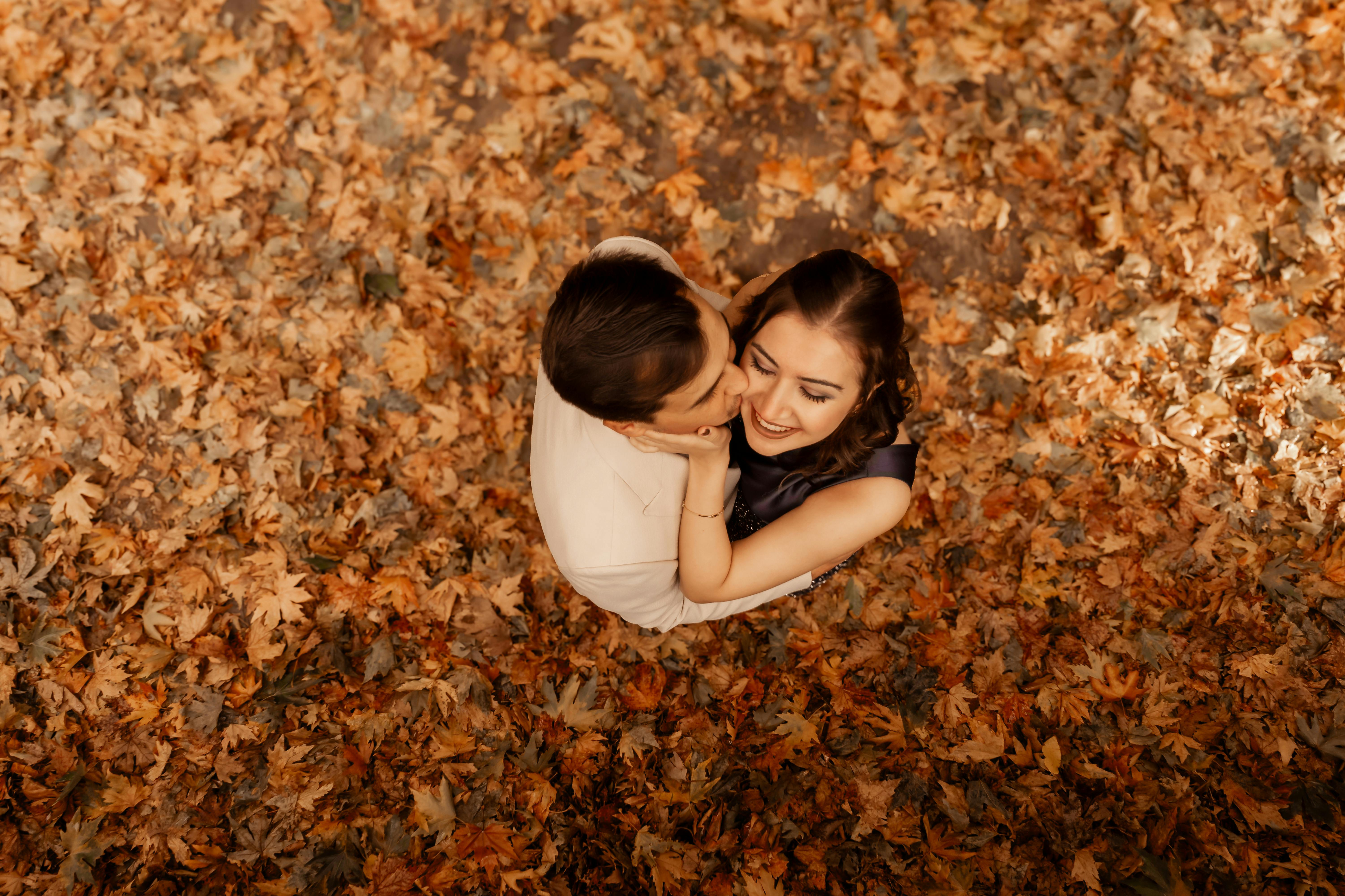 Loving couple embracing amidst fallen autumn leaves, soft earthy tones mirroring the storm's intimate embrace inside
