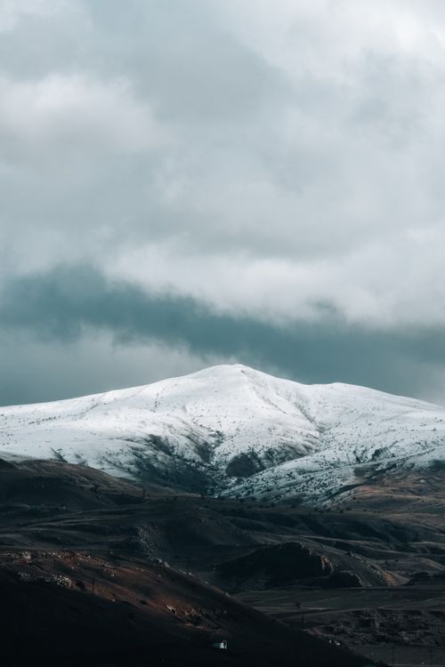 Free A snow-capped mountain stands majestically under a dramatic, cloudy sky. Stock Photo