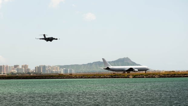 Photo by Roy Kim Military aircraft landing near Hawaiian coastline with cityscape backdrop.
