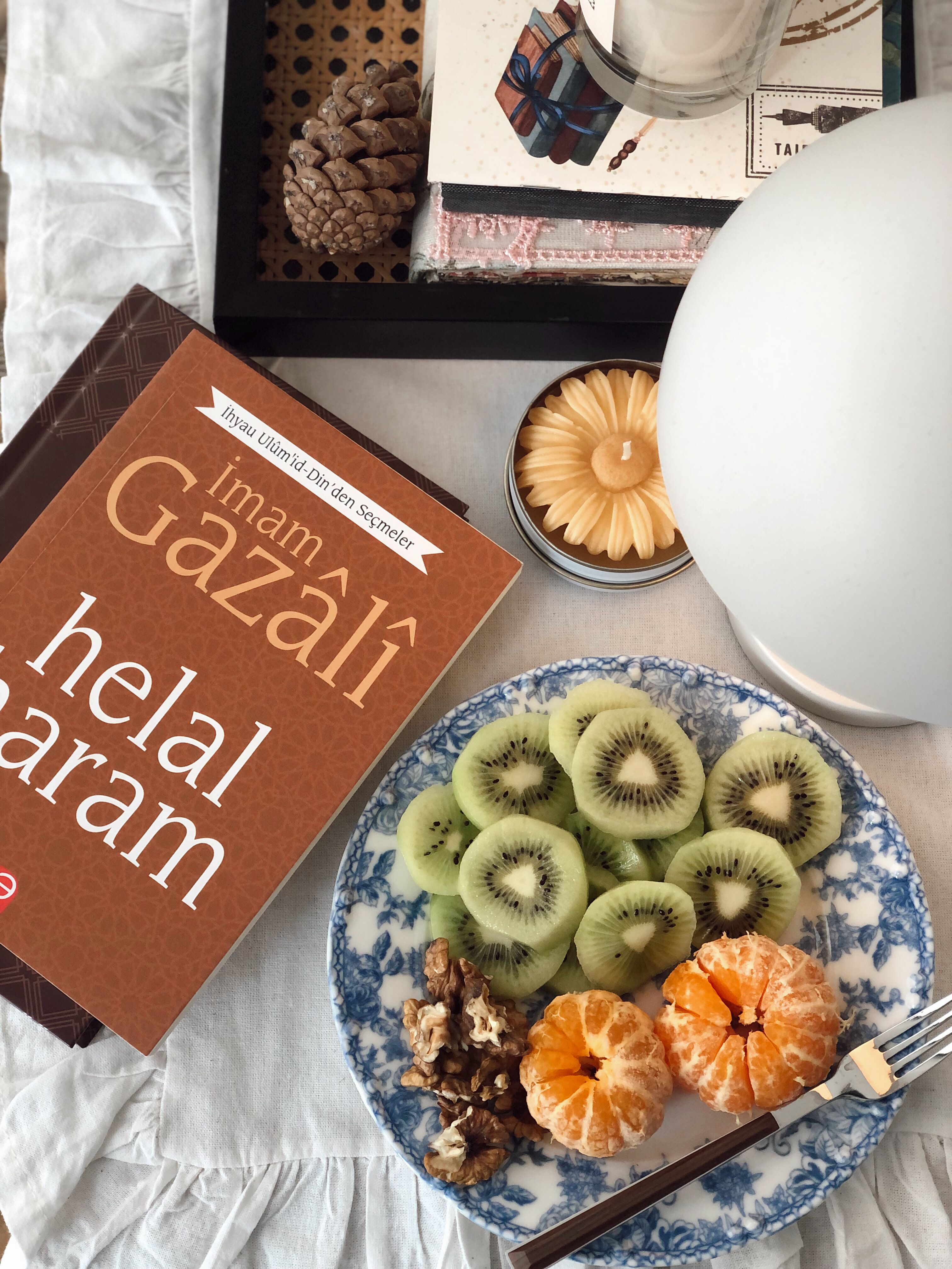 A flat lay featuring sliced kiwi, mandarin, a cultural book, and a candle.