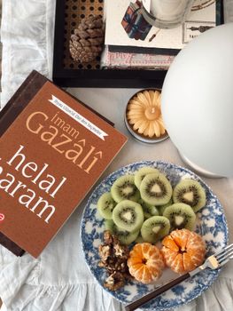 A flat lay featuring sliced kiwi, mandarin, a cultural book, and a candle.