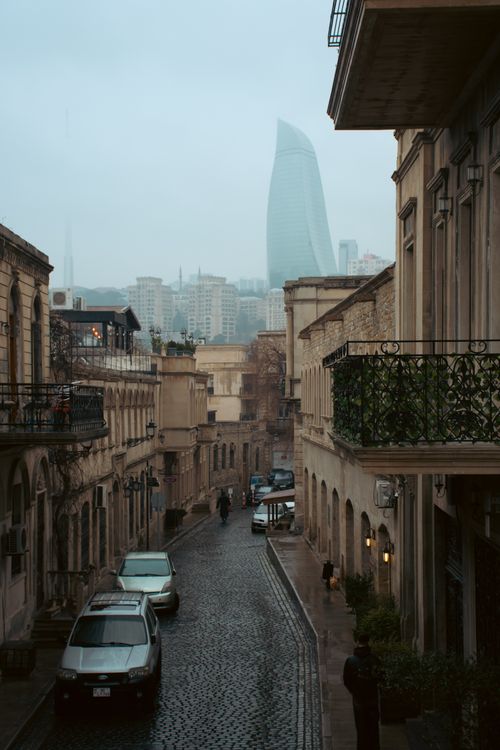 Free Rainy day in Baku showcasing historic architecture and a view of the Flame Towers from a cobblestone street. Stock Photo