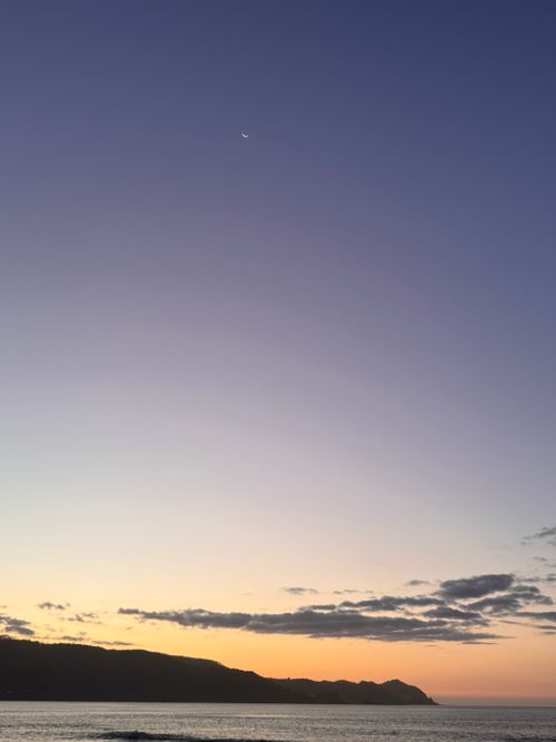 Free A tranquil seascape at twilight with gentle waves and a crescent moon in a clear sky. Stock Photo